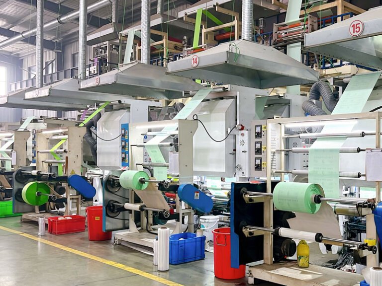 Large compostable film roll used for manufacturing portable toilet bags inside an industrial production facility with blown film equipment and sanitation bag materials