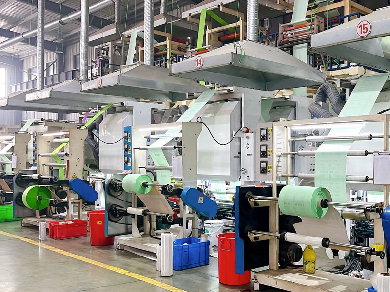 Large compostable film roll used for manufacturing portable toilet bags inside an industrial production facility with blown film equipment and sanitation bag materials